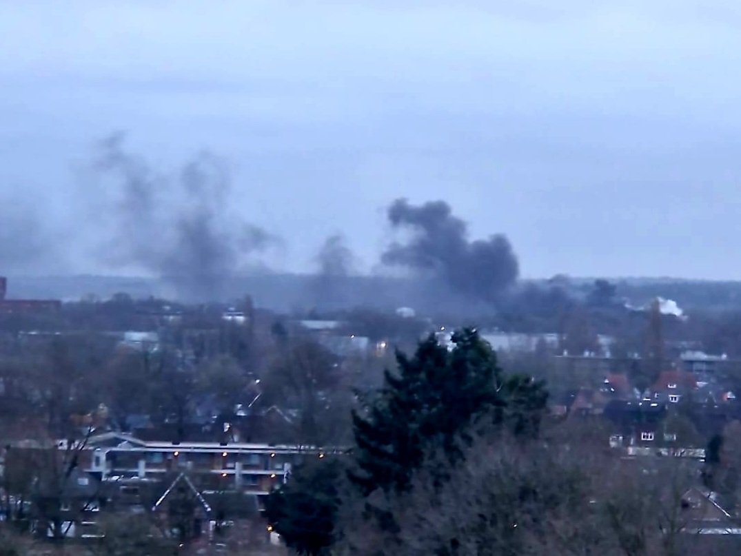 Zeecontainer in bedrijfshal in brand; grote rookwolken boven bedrijfshallen