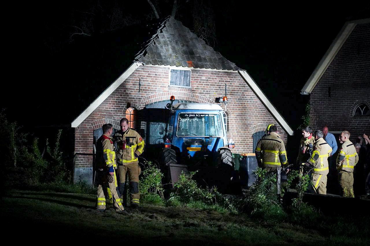 Brandende tractor start en rijdt tegen schuur aan