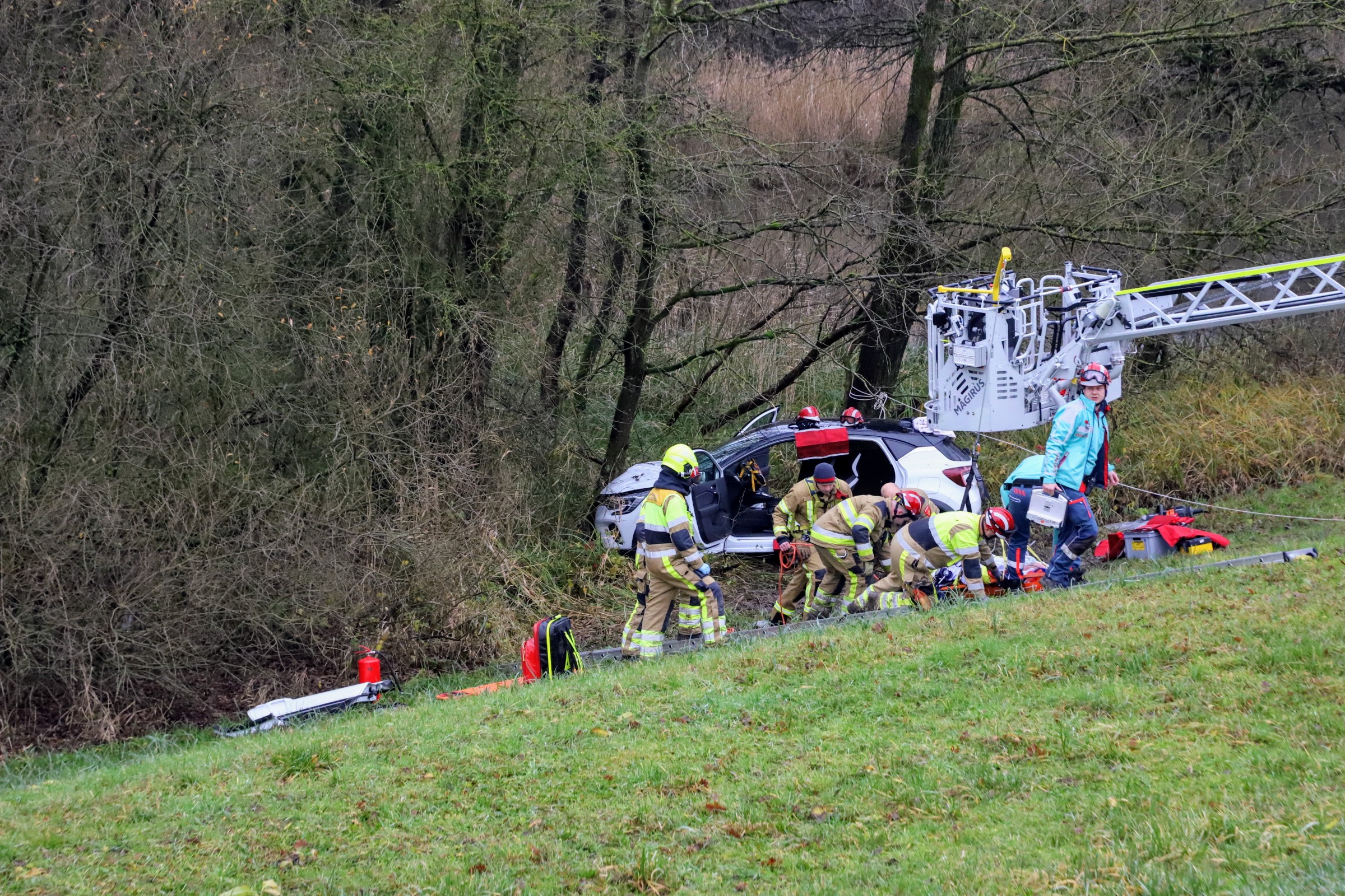 Auto rijdt van dijk en botst tegen boom, bestuurder bekneld